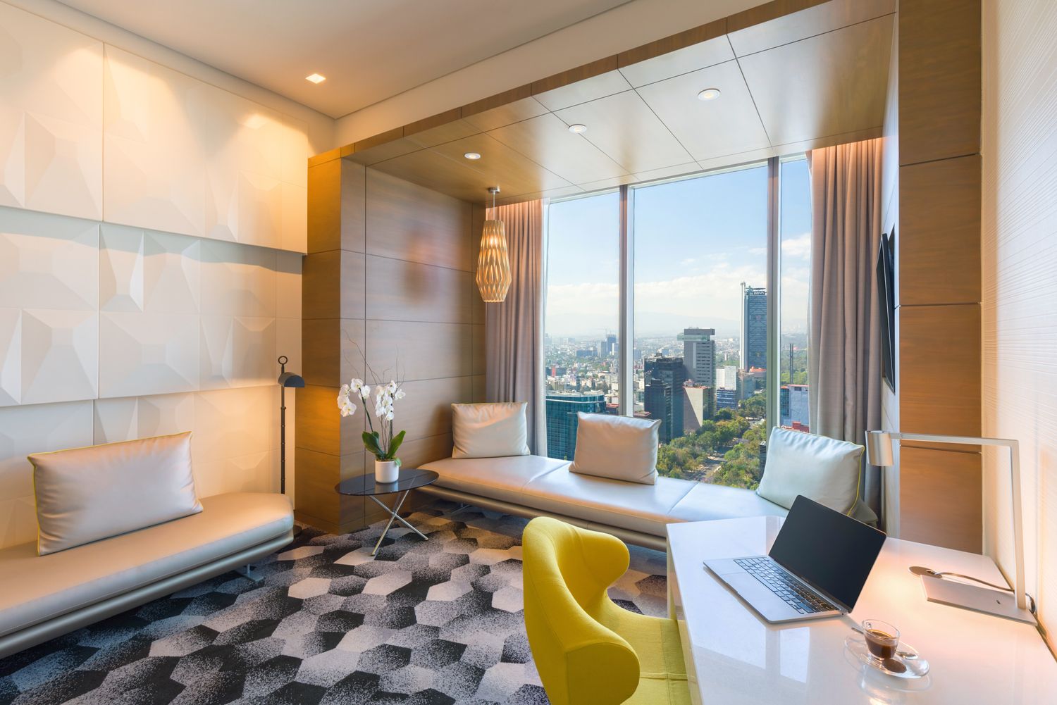 Luxurious modern hotel lounge area with yellow accent chair and panoramic city views through floor-to-ceiling windows.