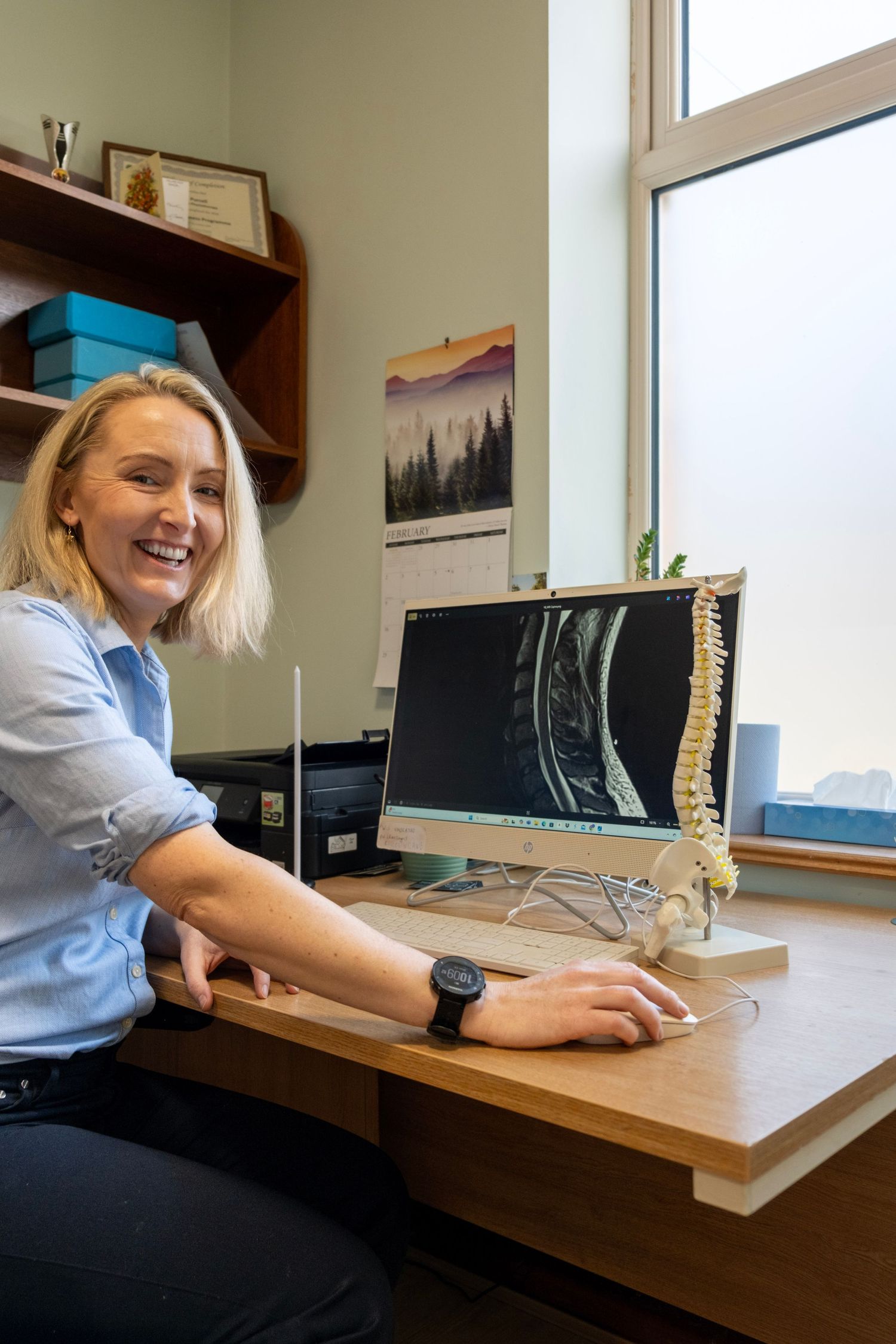 Physiotherapist sitting at her desk smiling while looking at an xray of a spine