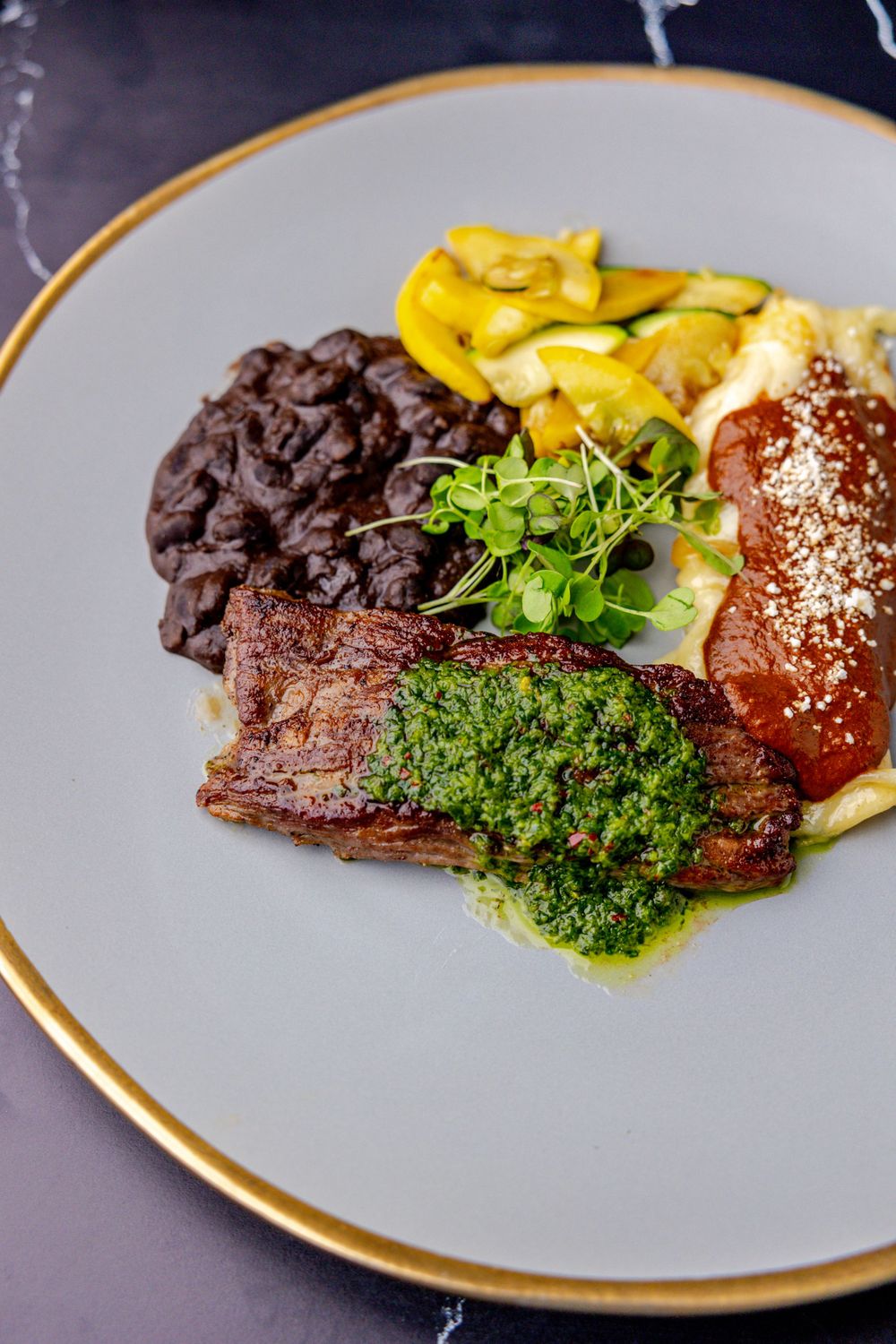 Elegant plated dish featuring meat with green herb garnish and yellow vegetables.