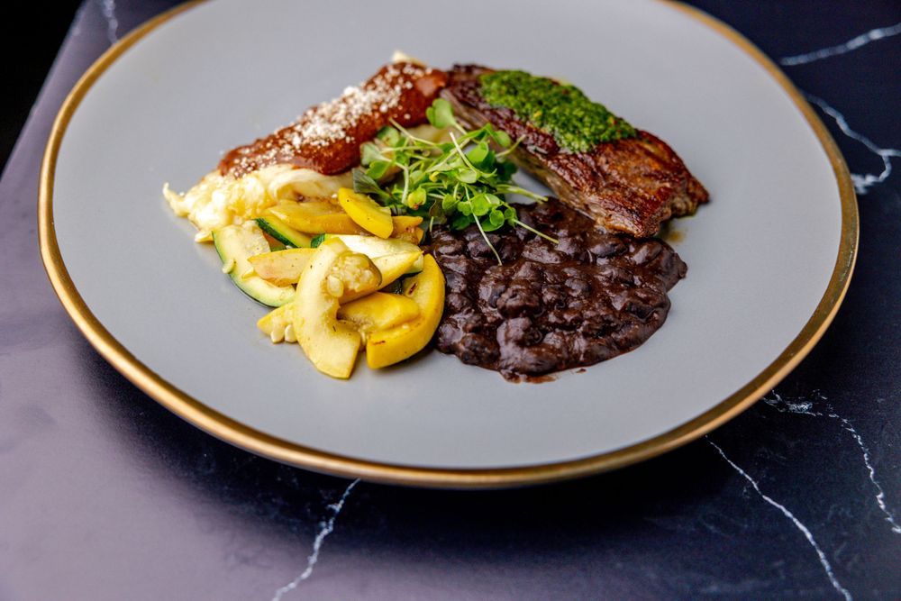 Fine dining plate presentation with braised meat, microgreens, and seasonal vegetables.