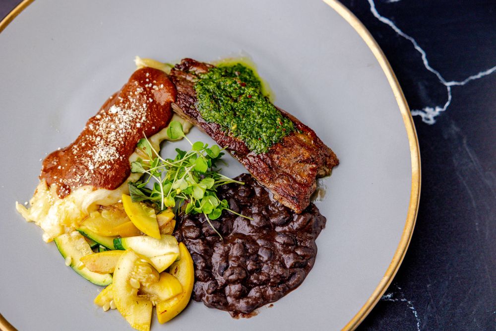 Grilled steak dish with vibrant microgreens and yellow garnish served on a dark plate with elegant plating.
