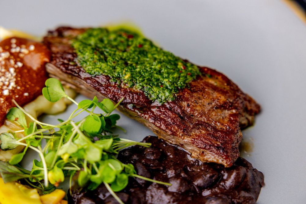 Perfectly cooked steak with fresh herbs and colorful accompaniments on an elegant black plate.