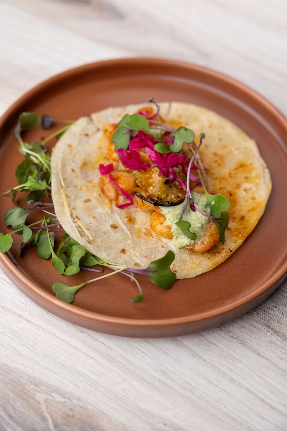 Artisanal tacos garnished with bright microgreens and edible flowers on a terracotta plate.