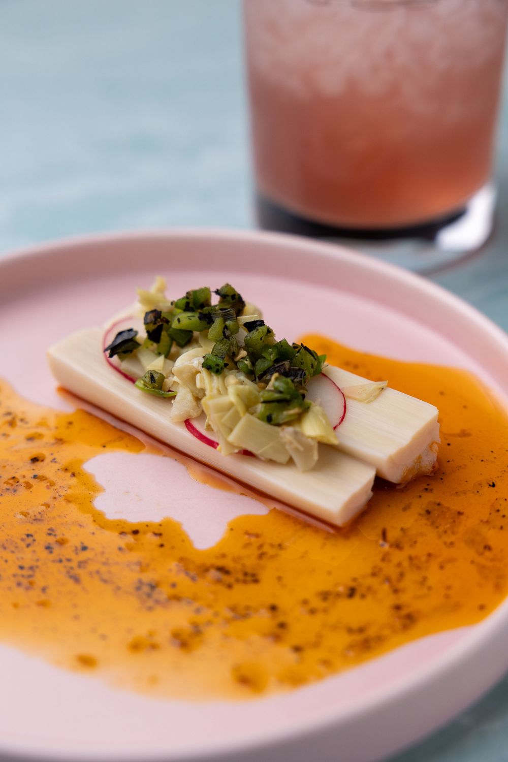 Creamy orange soup with sliced cheese and herb garnish in a modern pink bowl.
