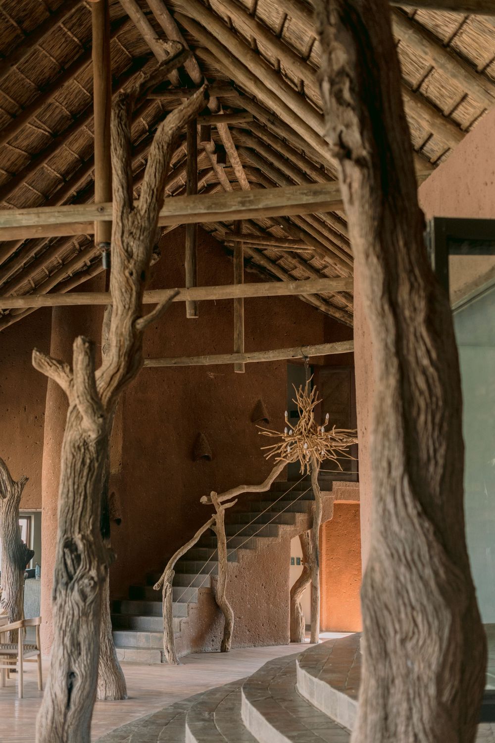 Rustic safari lodge interior with natural wood beams, thatched roof, and organic branch chandelier.