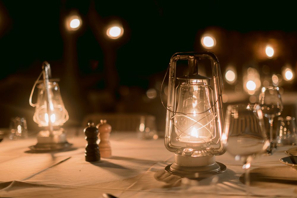 Vintage kerosene lanterns glowing warmly on an outdoor safari dinner table at night.