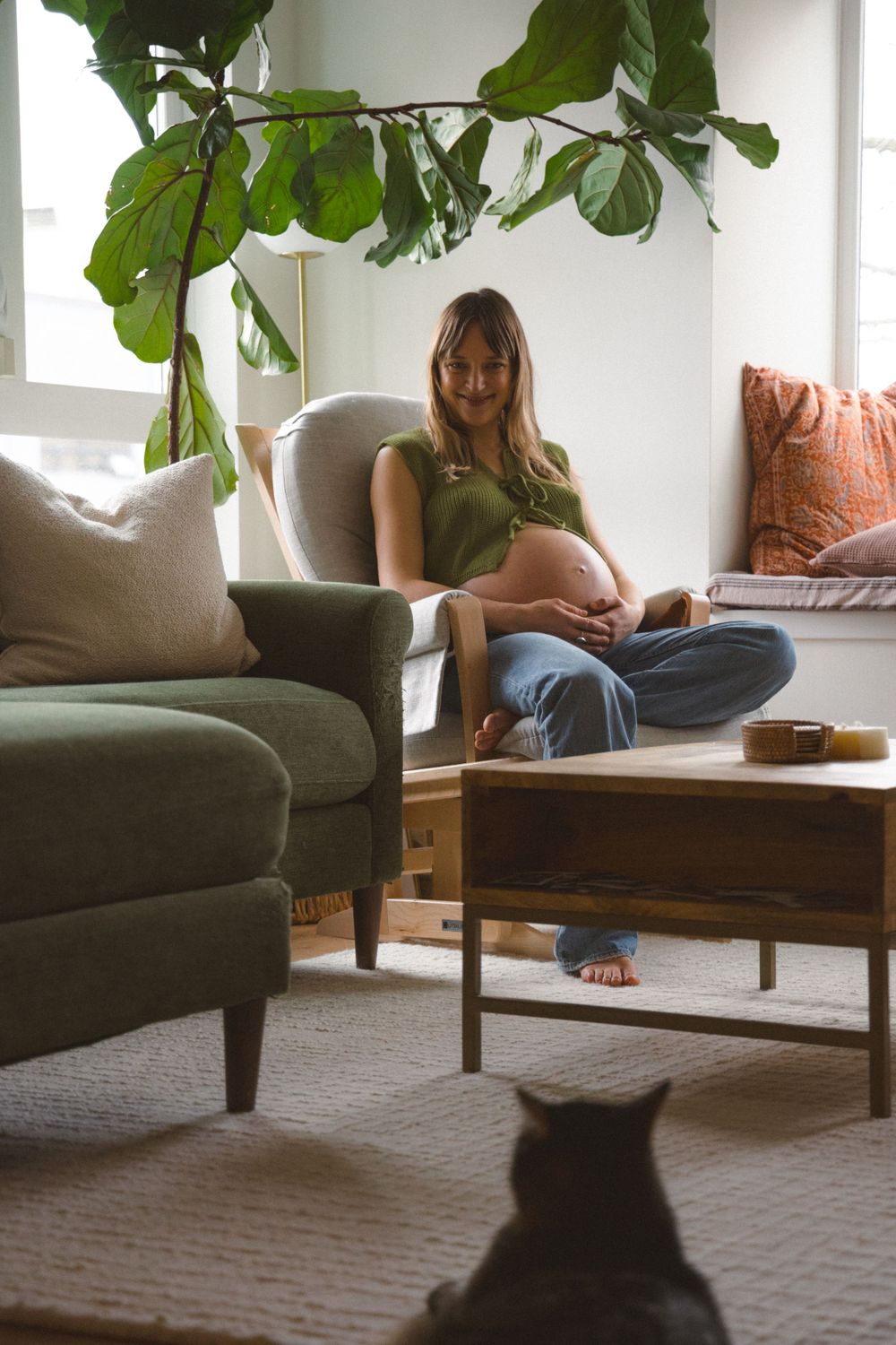 expecting mom sitting in her rocking chair in her living room wearing a colourful cropped knit top during a maternity session in vancouver.