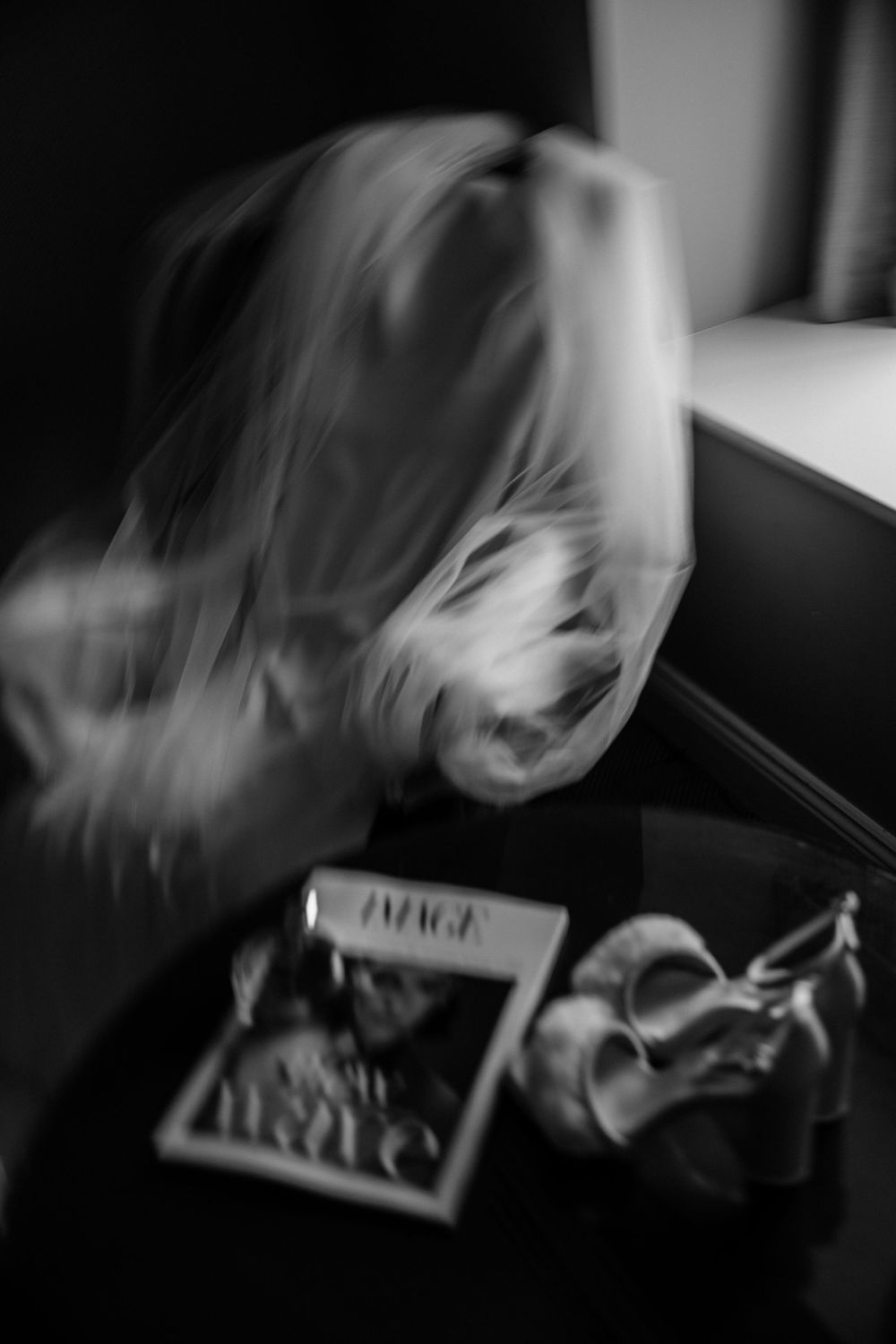 Blurry black and white motion photo of someone with long hair next to a magazine and glasses on table.