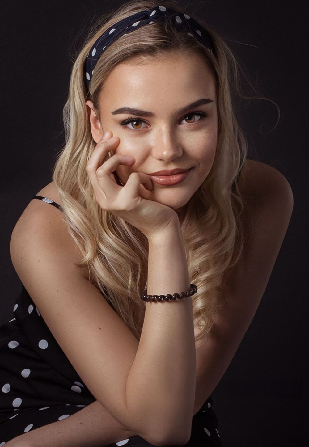 Portrait of person in polka dot dress with blonde hair and retro-style headband.