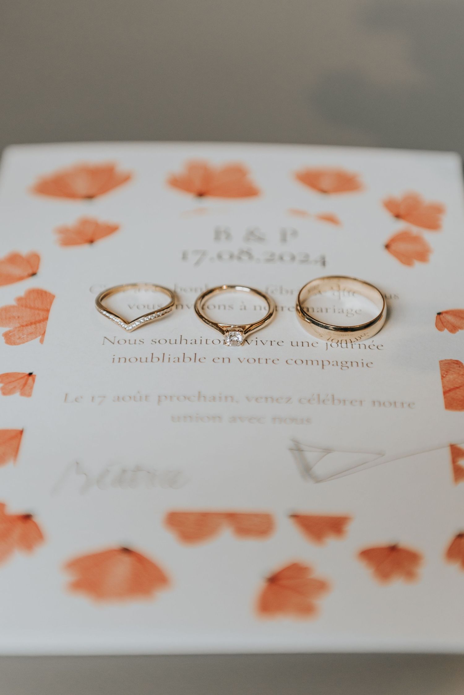 Three gold wedding rings arranged on a white invitation card with coral-colored floral accents.