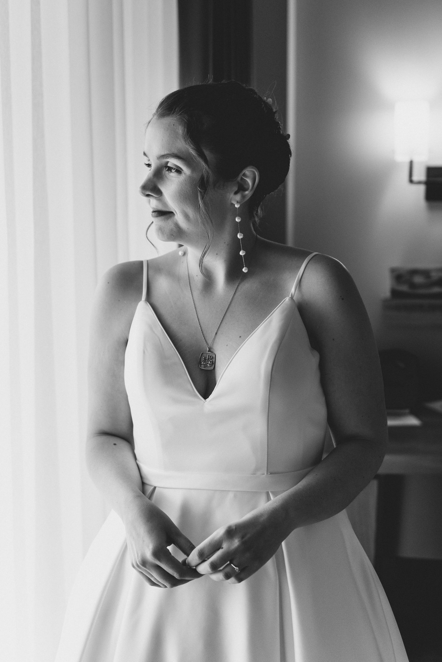 A black and white portrait of a person in a white bridal gown by a window with natural light.