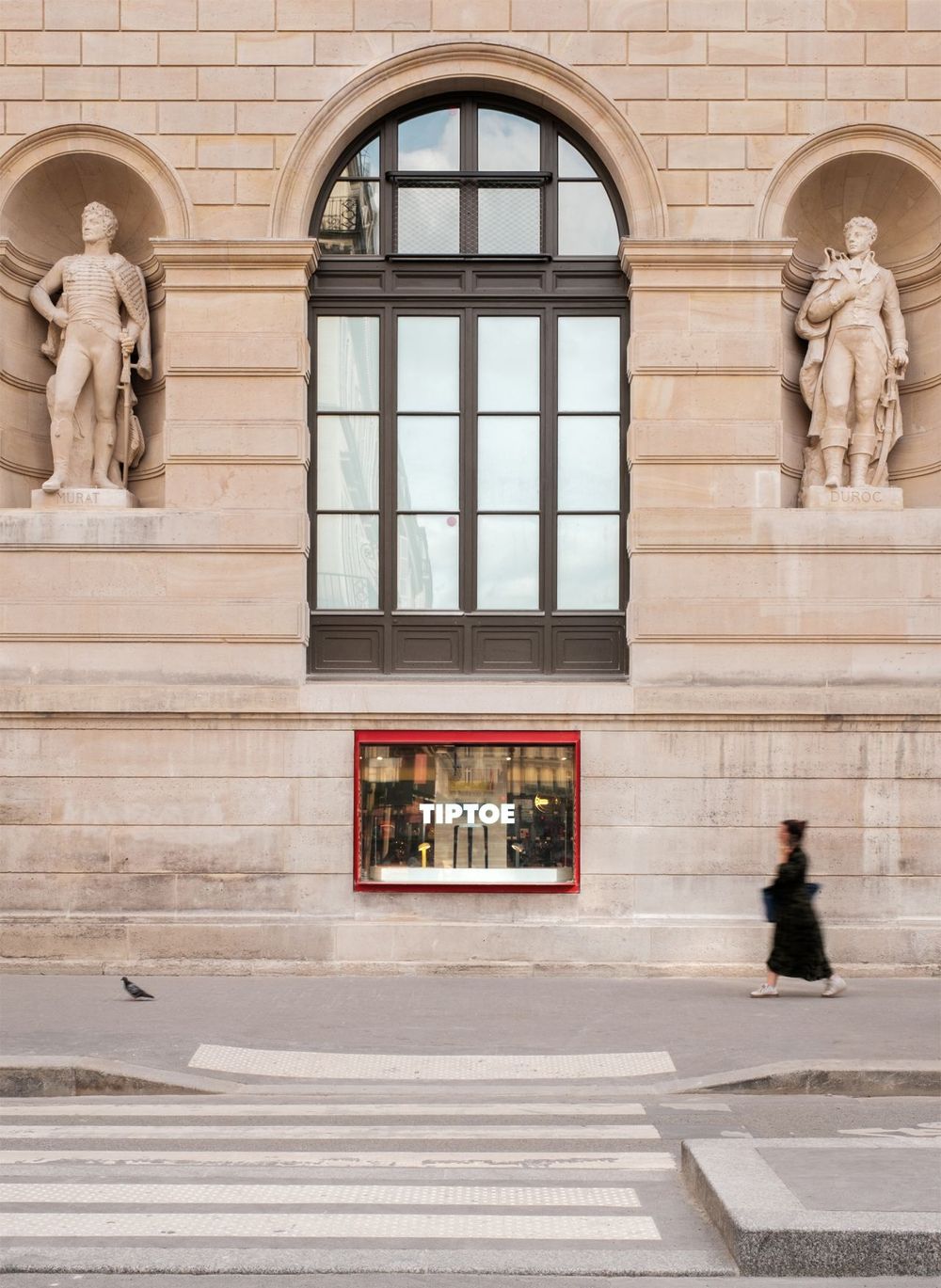 Classical building facade with arched window and sculptural niches displaying statues.