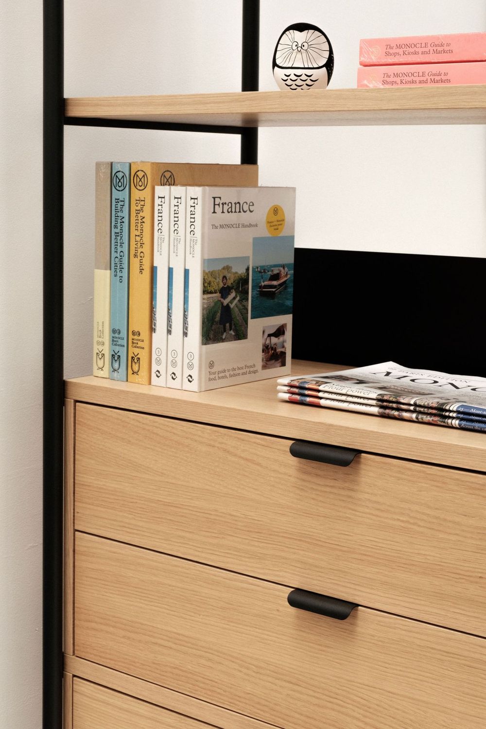 Wooden shelf unit with books and drawers featuring black handles.