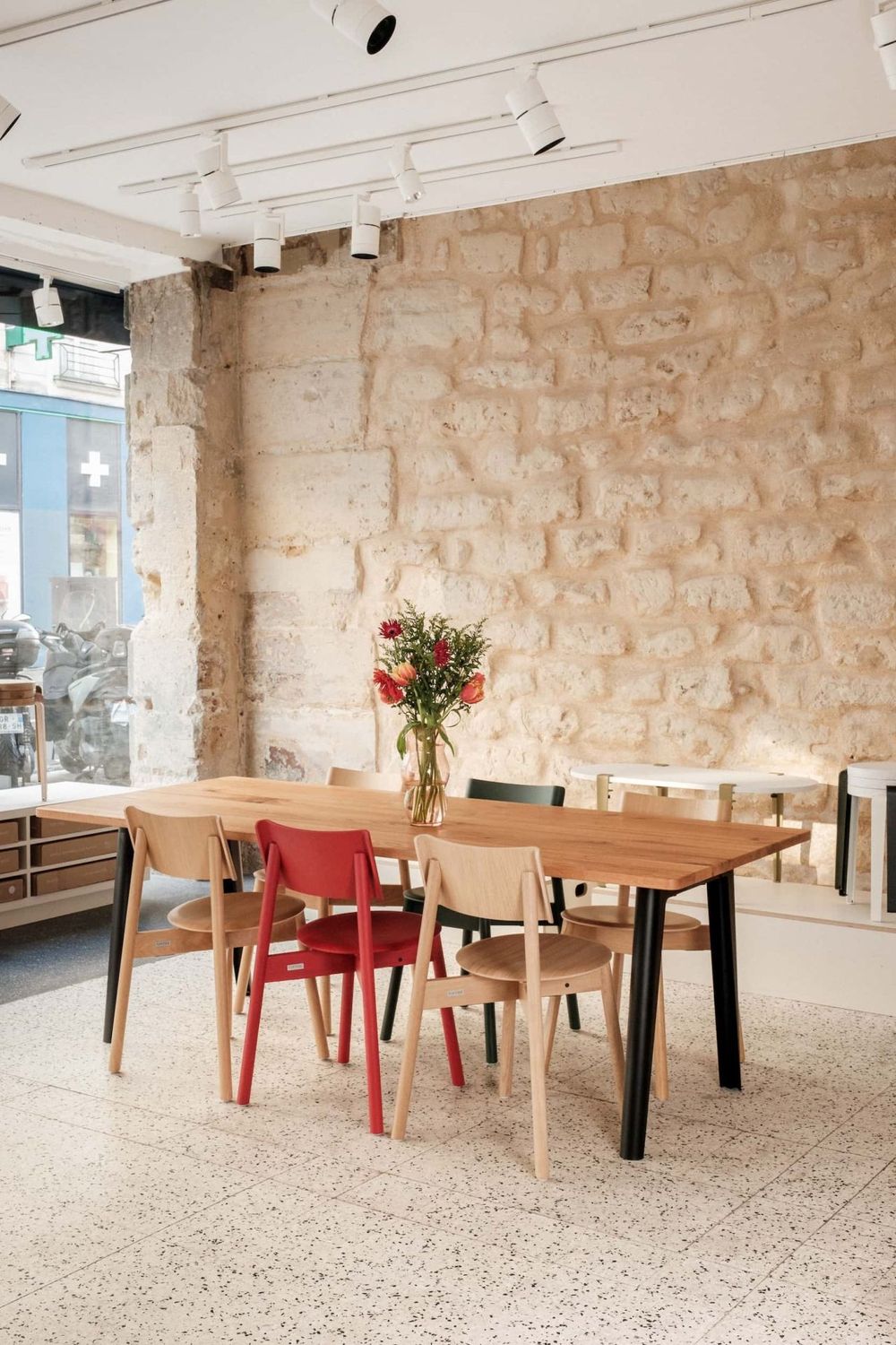 Modern dining area with wooden table, mixed chairs and exposed stone wall decorated with fresh flowers.
