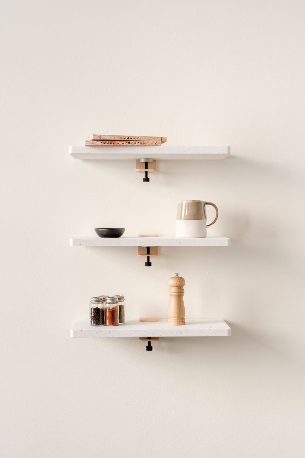 Three white floating shelves with minimalist decor including books, mug and spice jars.
