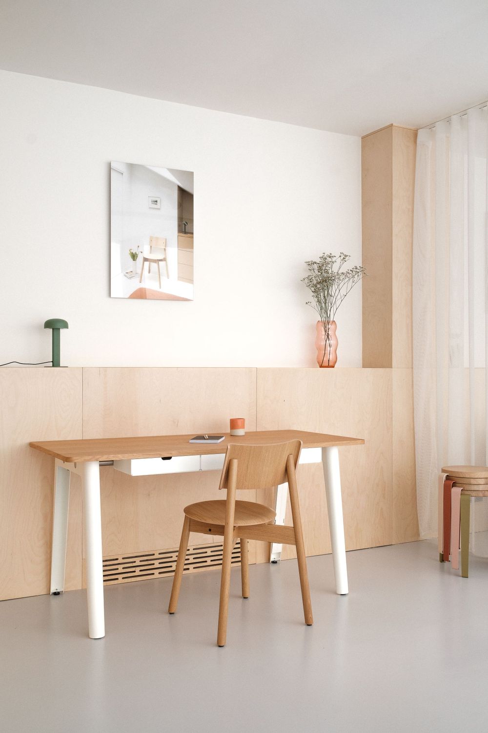 Minimalist home office with wooden desk, beige chair and decorative wall art.