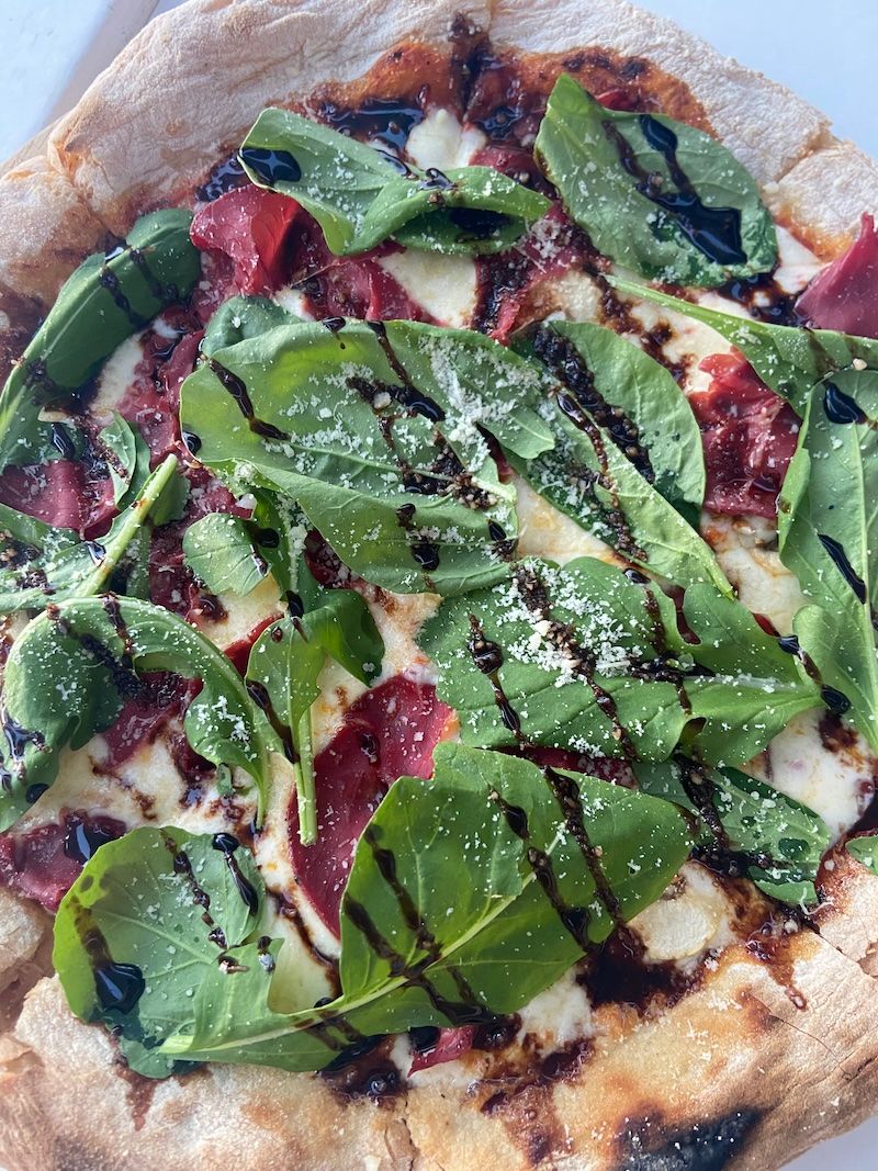 Gourmet pizza topped with fresh arugula, prosciutto, parmesan cheese and balsamic glaze on a thin crust.