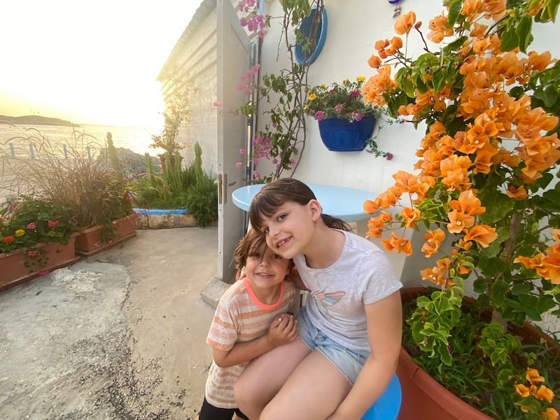 A garden patio decorated with vibrant orange flowers in hanging baskets and potted plants at sunset.