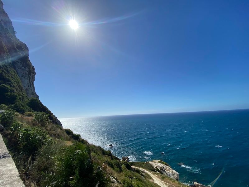 Stunning coastal view with bright sun over blue ocean waters along rocky cliffs on a clear day.