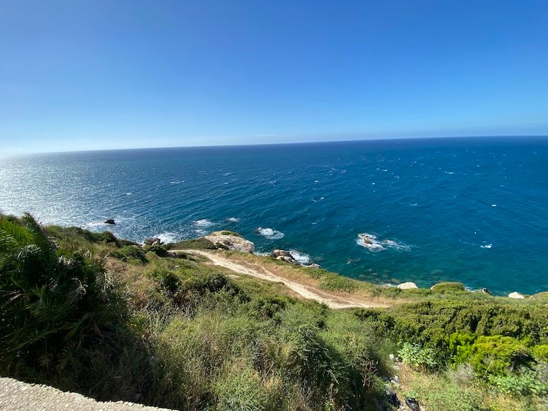 Scenic coastal view of turquoise waters and rocky shoreline along green hillside under bright blue sky.