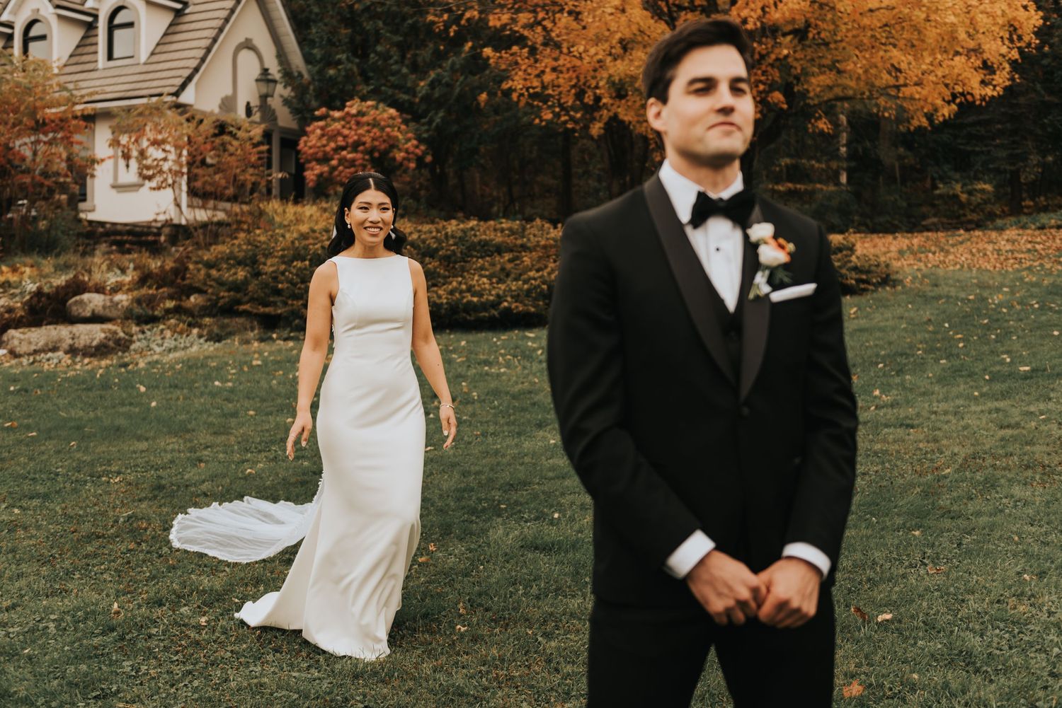 A romantic first look moment at an autumn wedding with colorful fall foliage and a white house in the background.