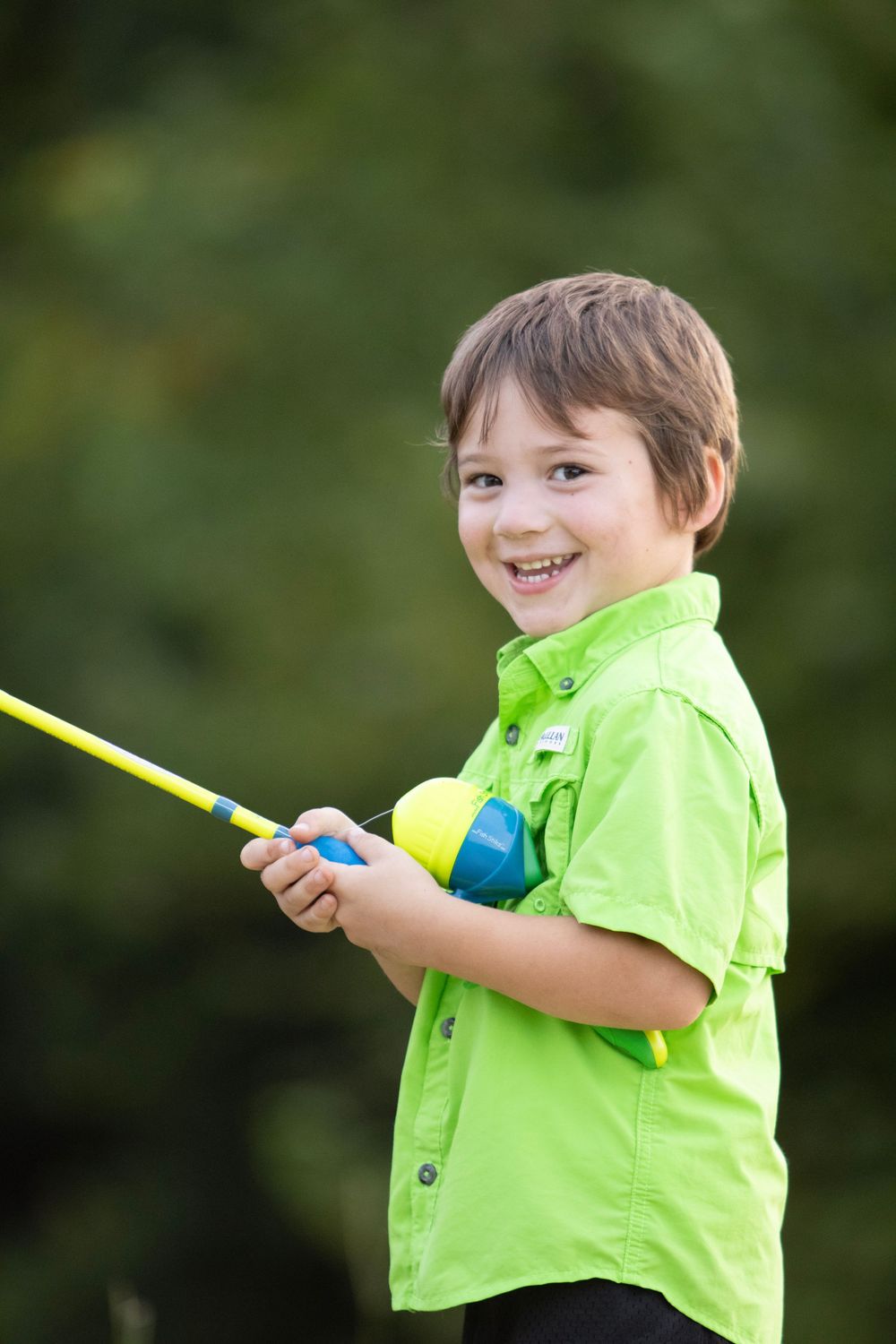 Child in bright green shirt plays outdoors with a colorful toy against a natural green background.