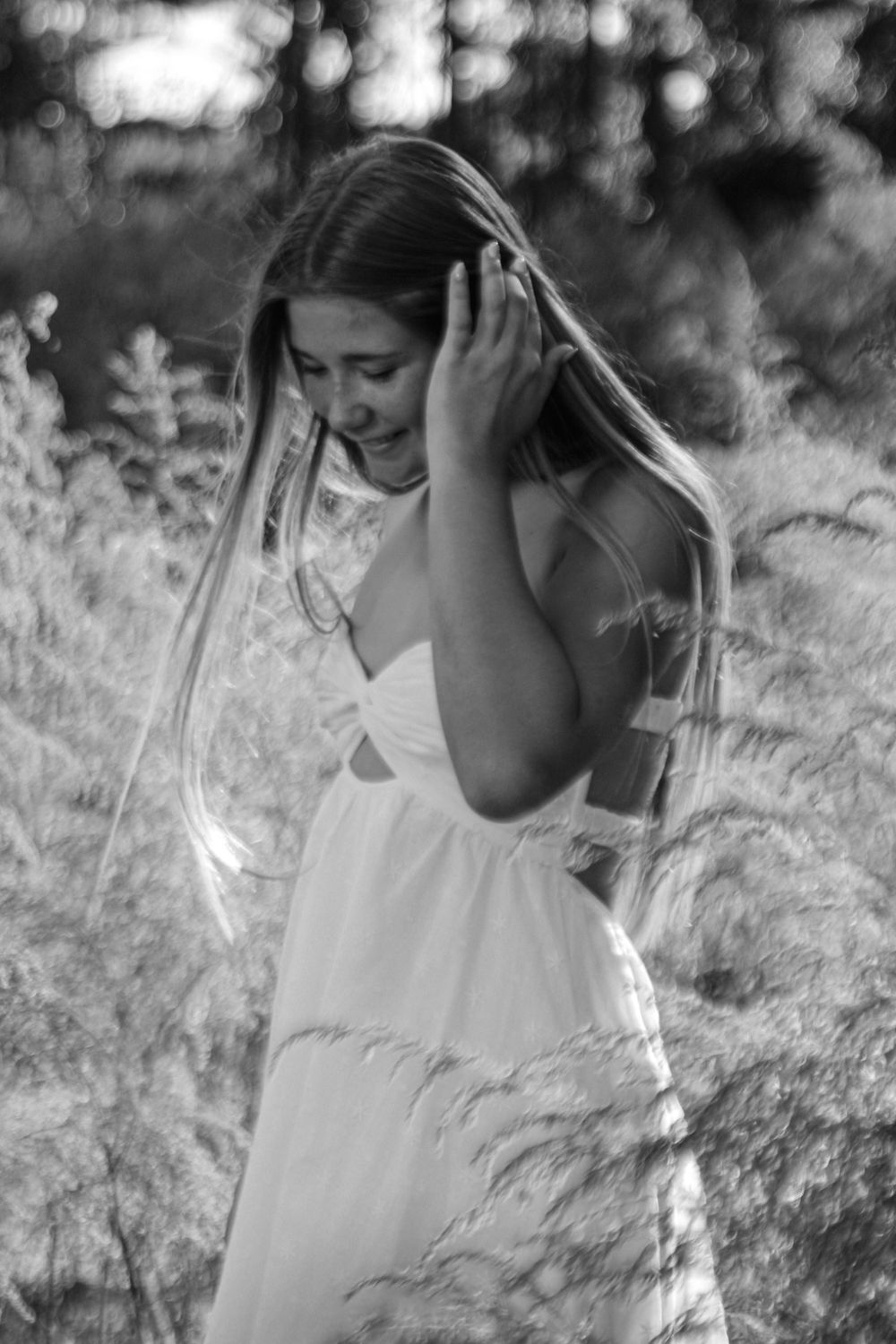 Black and white photo of someone in a flowing white dress touching their hair in a field.