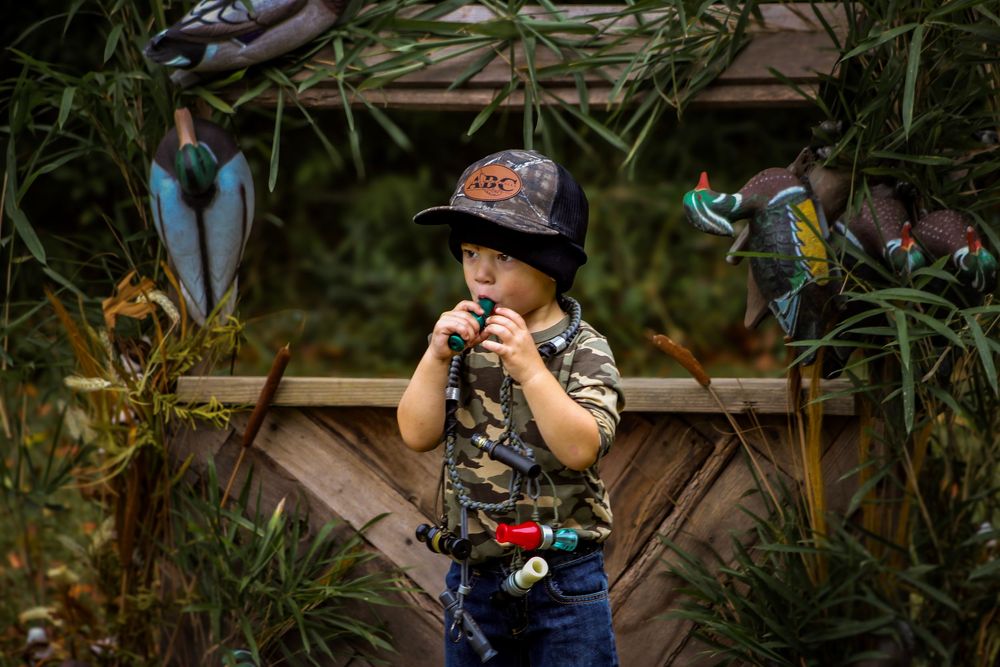 Young child wearing a baseball cap holds up binoculars while exploring outdoors in a nature setting.