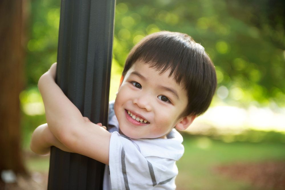 Cheerful toddler hugging a pole in a green Toronto park, captured by Phoebe Lee Photo