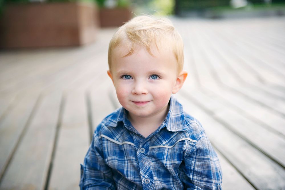 Blonde toddler in a blue plaid shirt standing on a wooden deck, photographed by Phoebe Lee Photo in Toronto