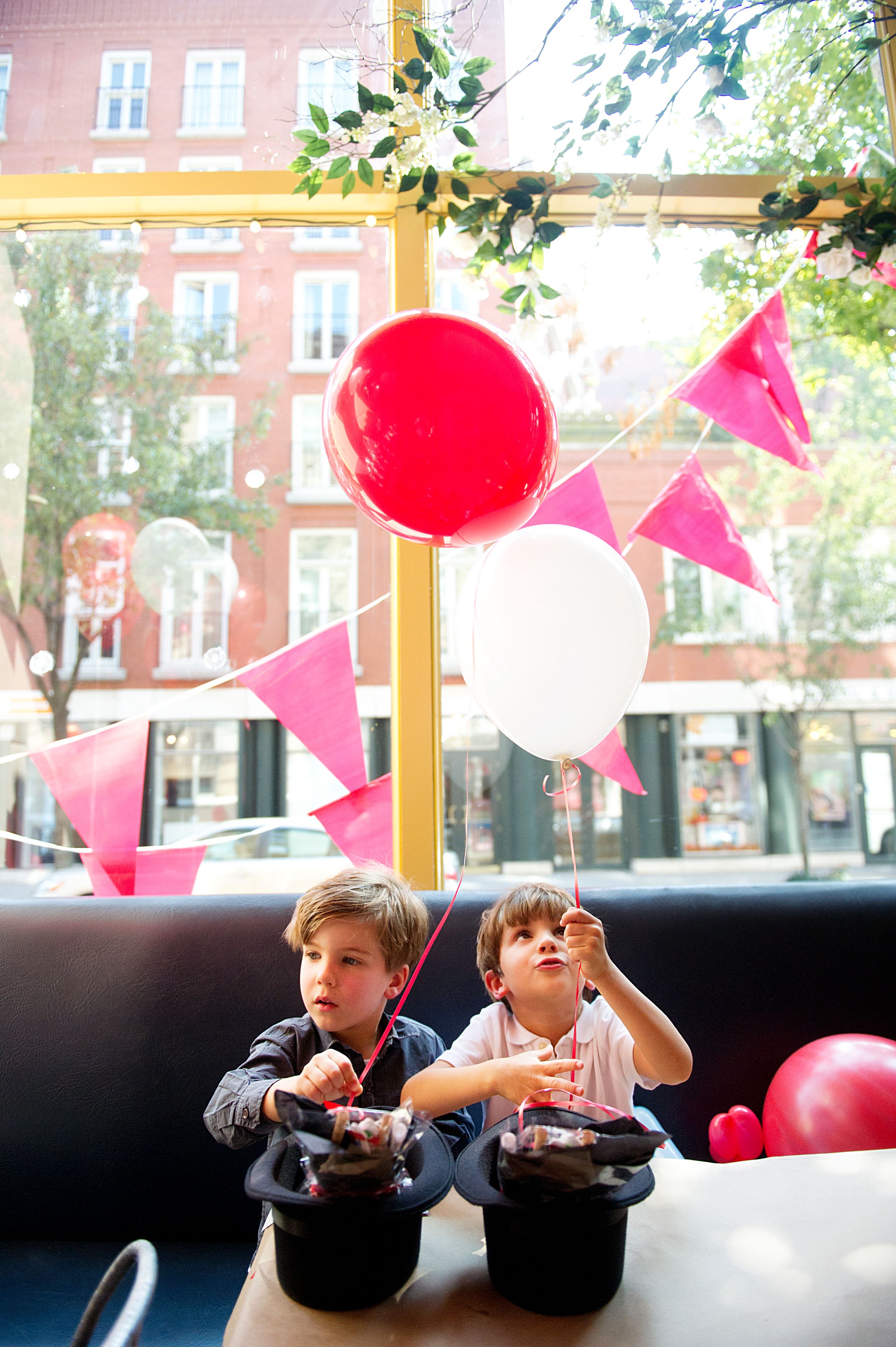 Two young boys sitting by a restaurant window with colorful balloons, photographed by Phoebe Lee Photo in downtown Toronto