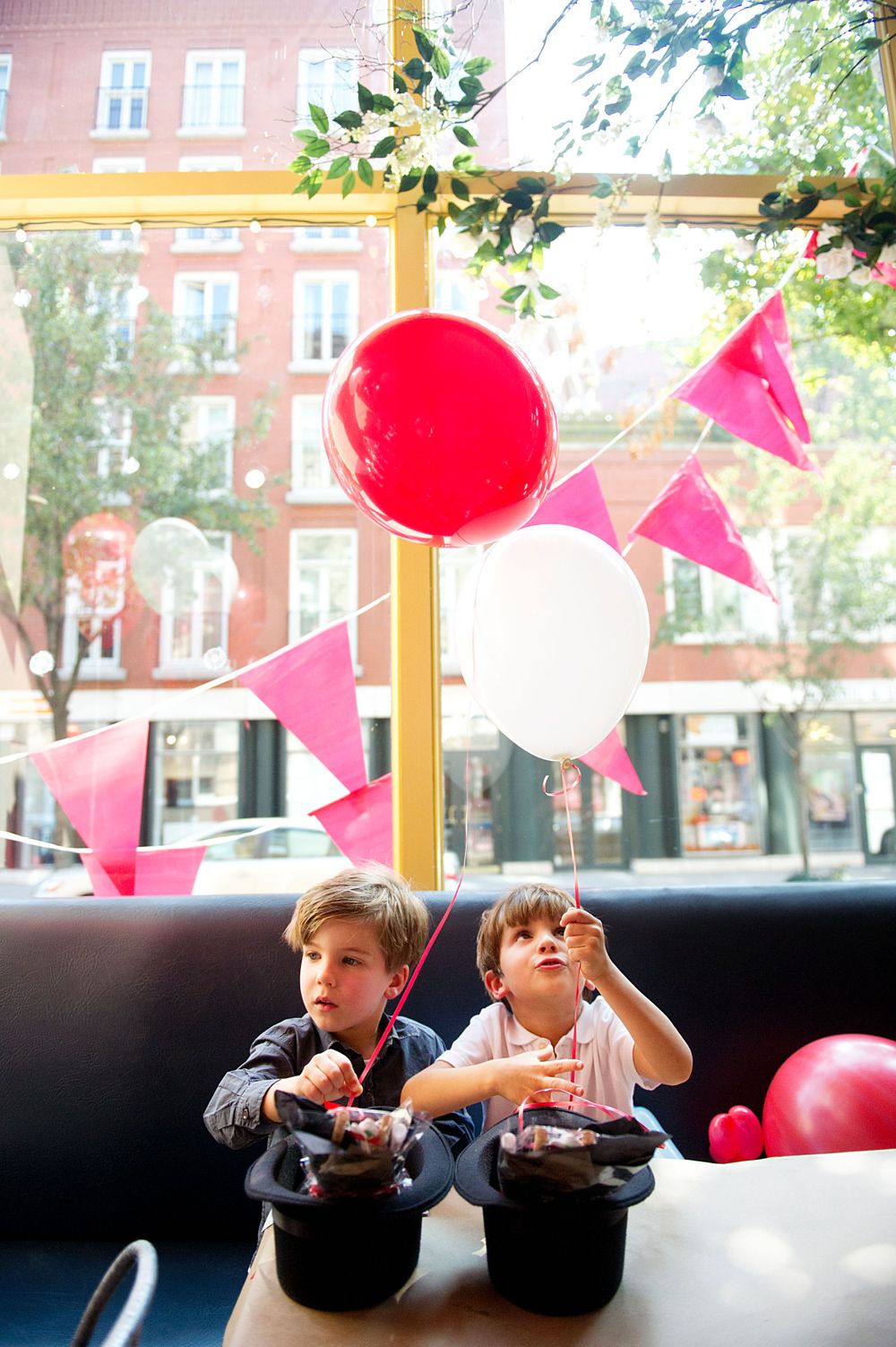 Two young boys sitting by a restaurant window with colorful balloons, photographed by Phoebe Lee Photo in downtown Toronto