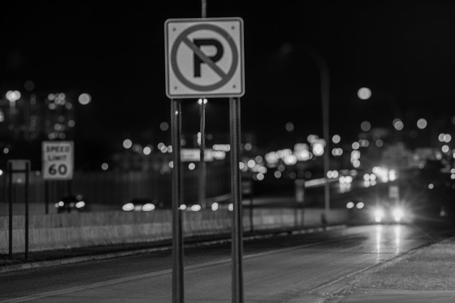 No parking sign illuminated at night with blurred city lights in background.