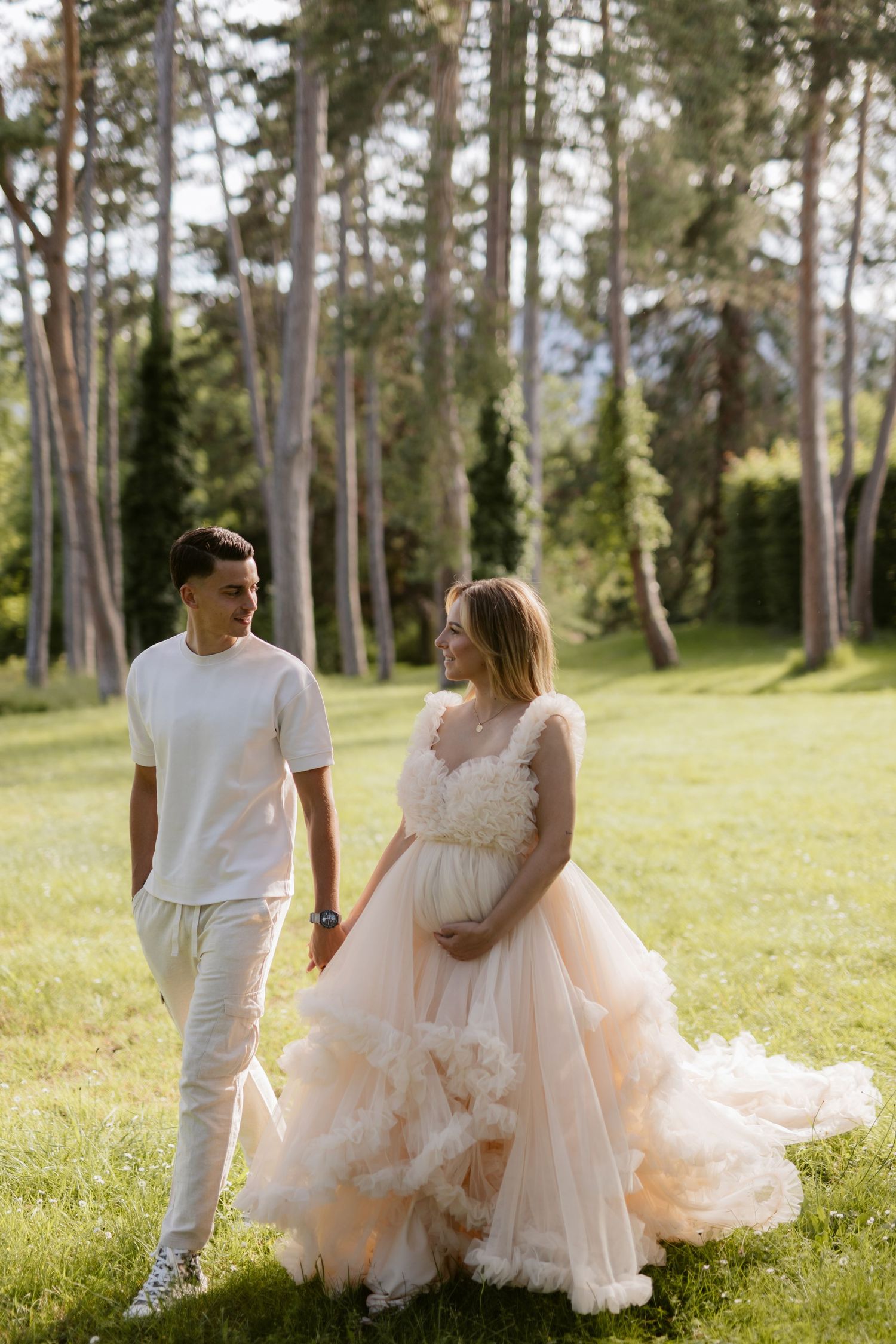 Dreamy engagement session with flowing white dress in sunlit pine forest.