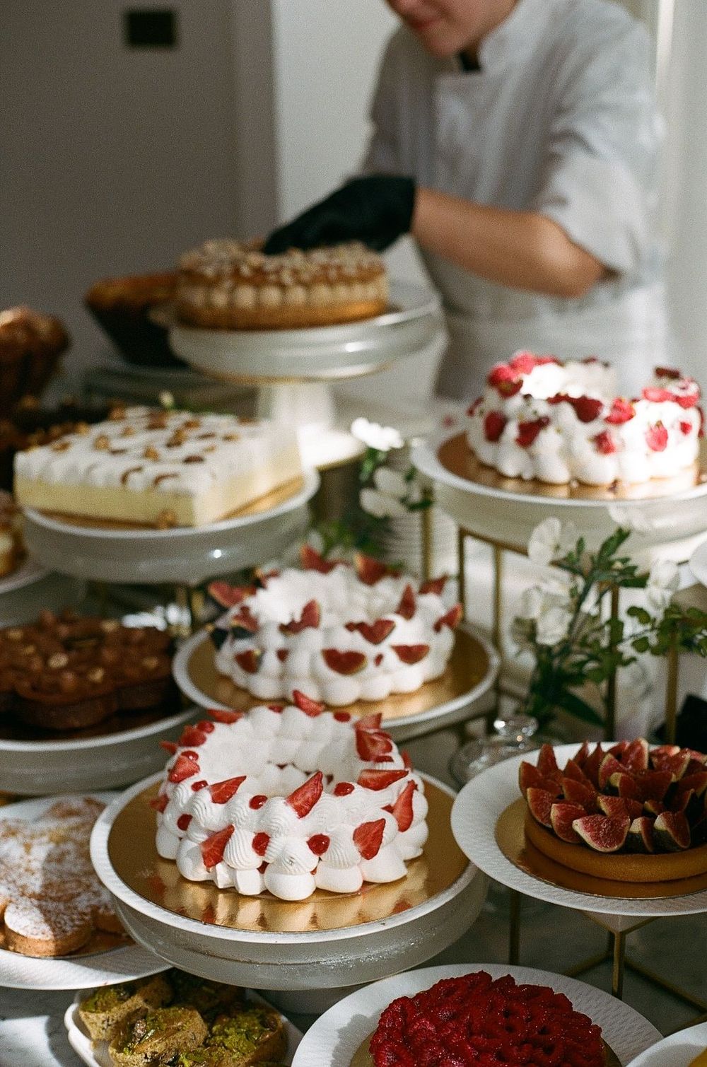 A display of elegant desserts featuring cream-topped cakes with strawberries, chocolate tarts, and various pastries on white plates.