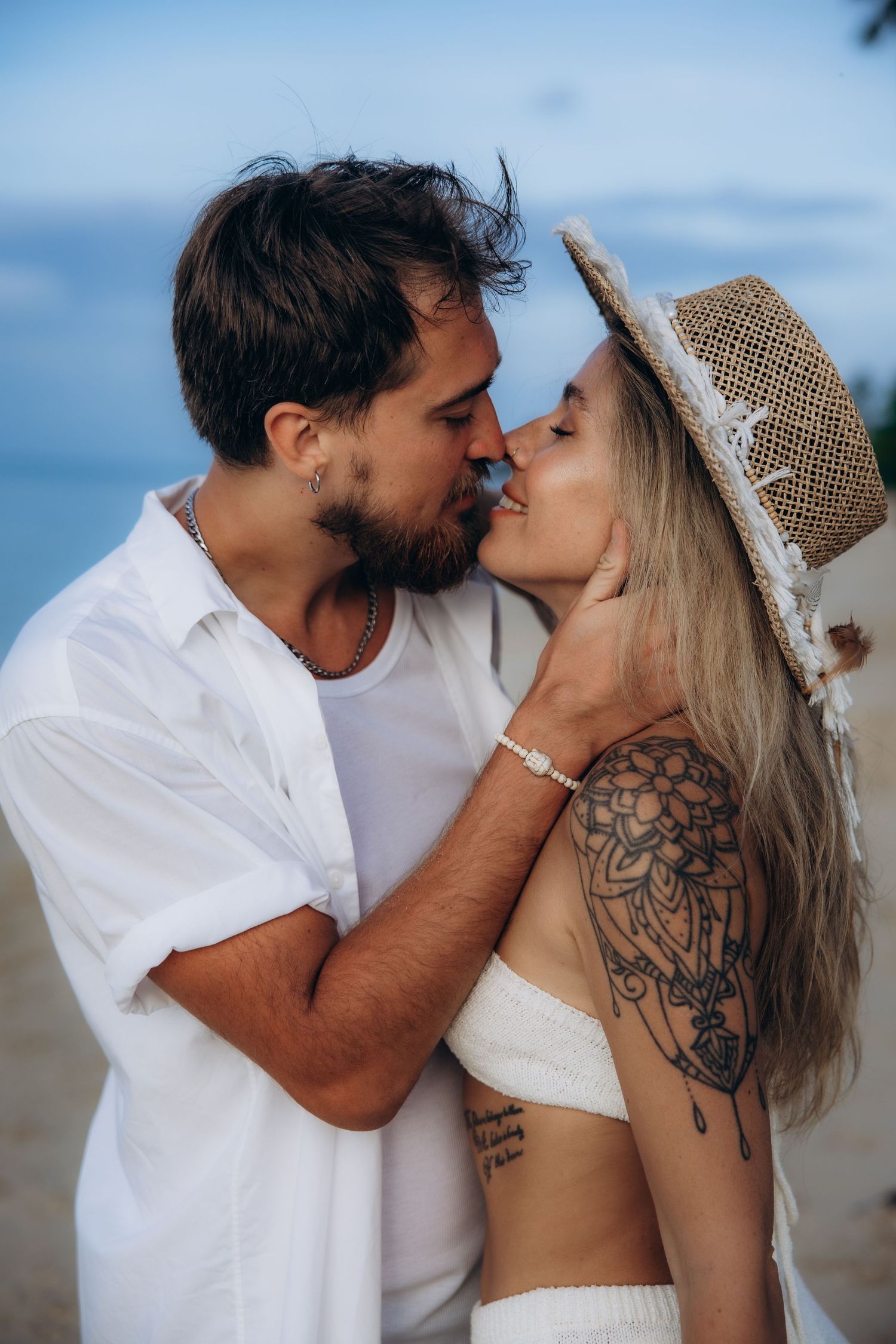A romantic beach scene showing two people sharing a kiss, with one wearing a straw hat and white clothing.