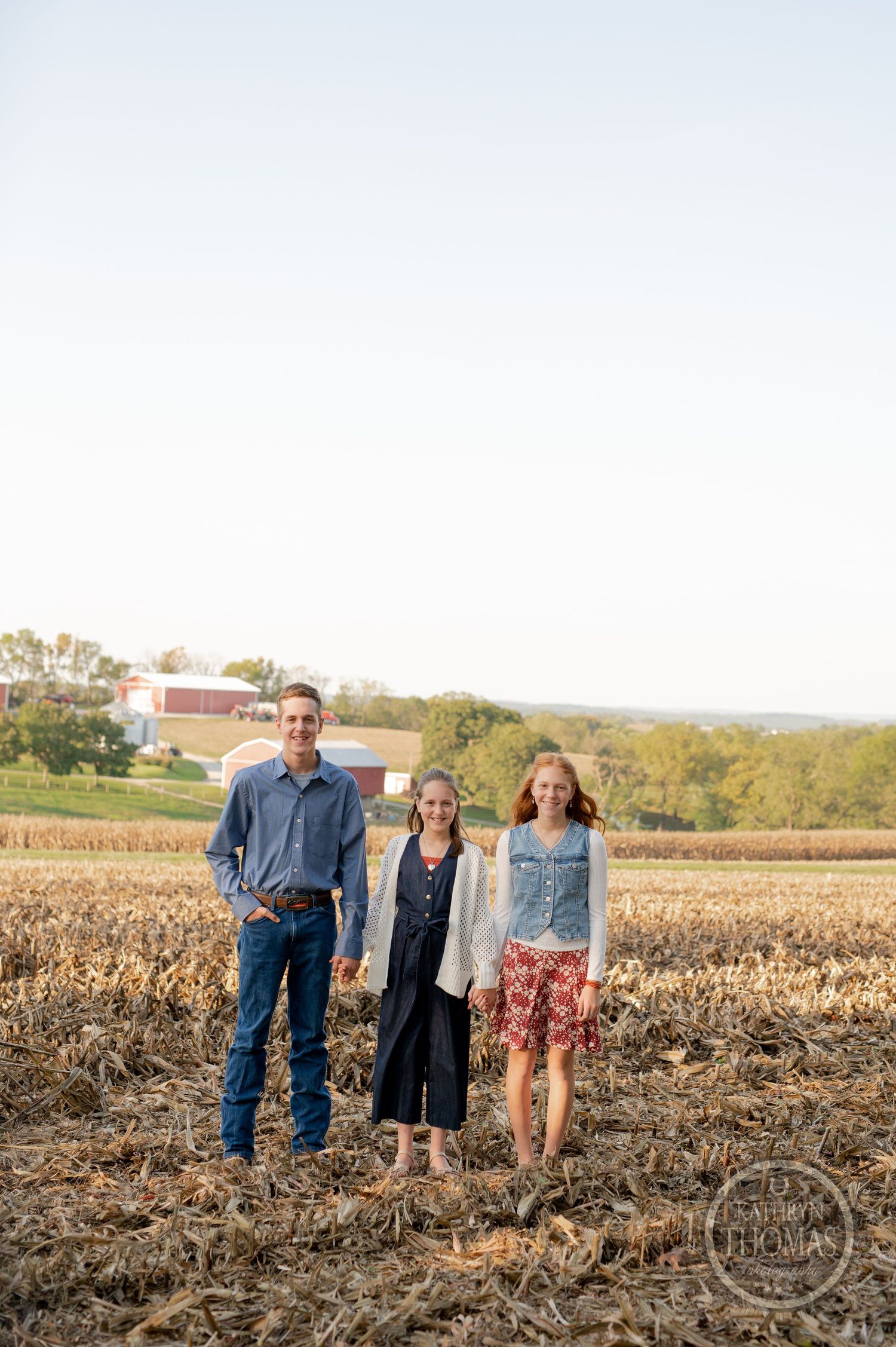 Three people standing in a harvested cornfield during golden hour.