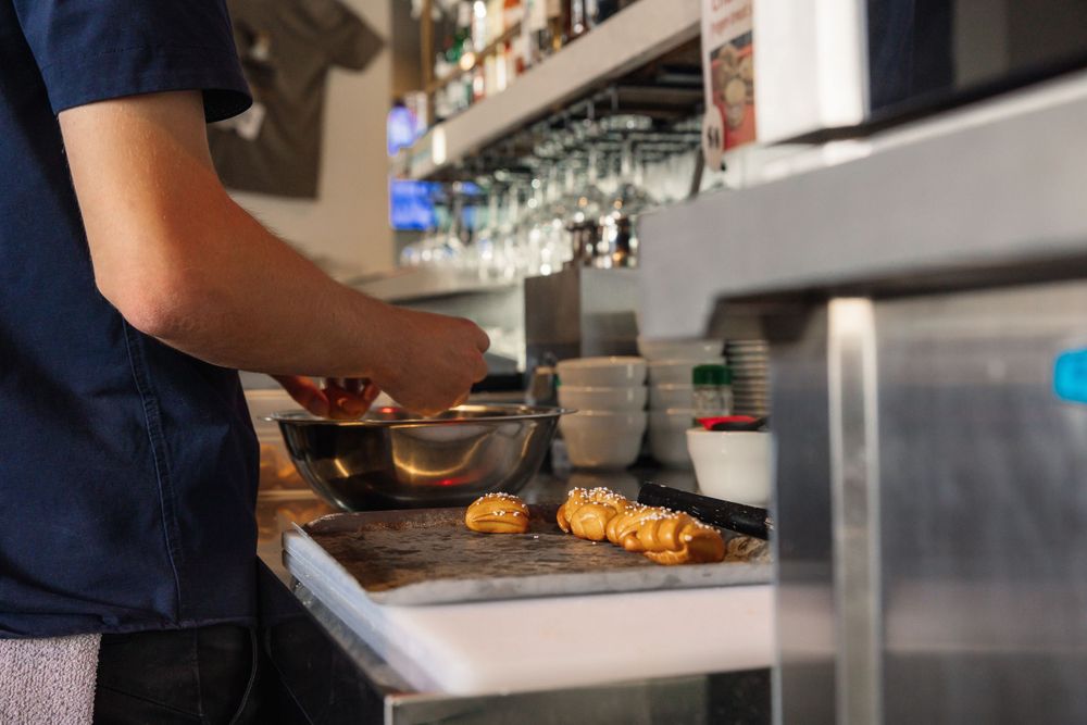 Chef preparing food in a commercial kitchen with glasses and equipment visible.