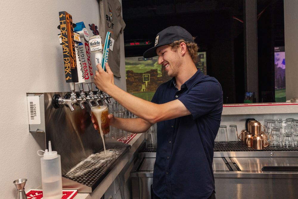 Restaurant worker operating drink taps behind a bar counter.