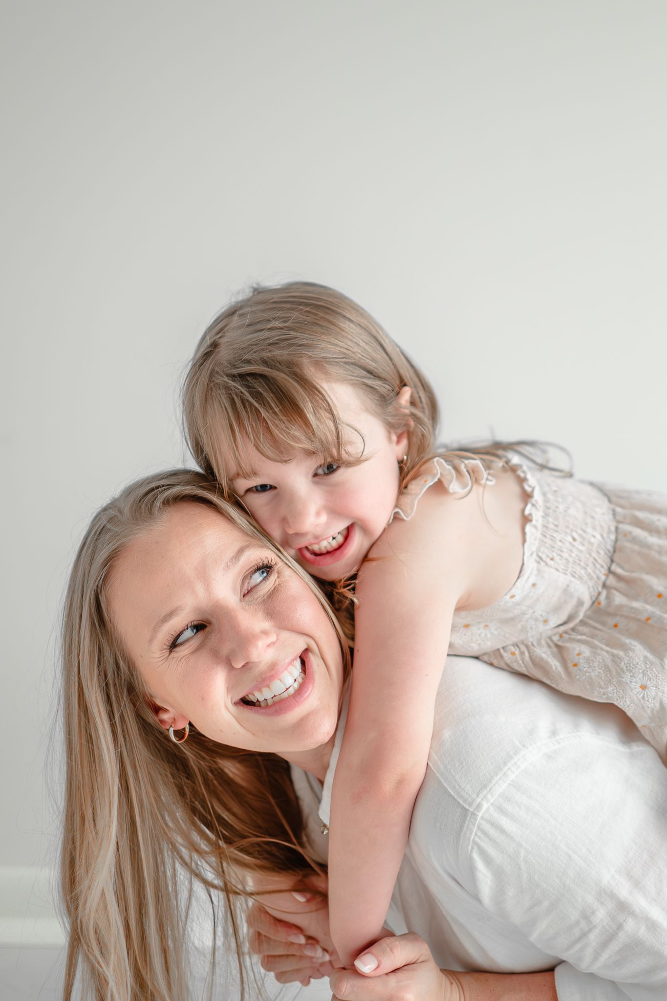 A joyful moment shared between two people wearing white as they embrace and laugh together against a light background.