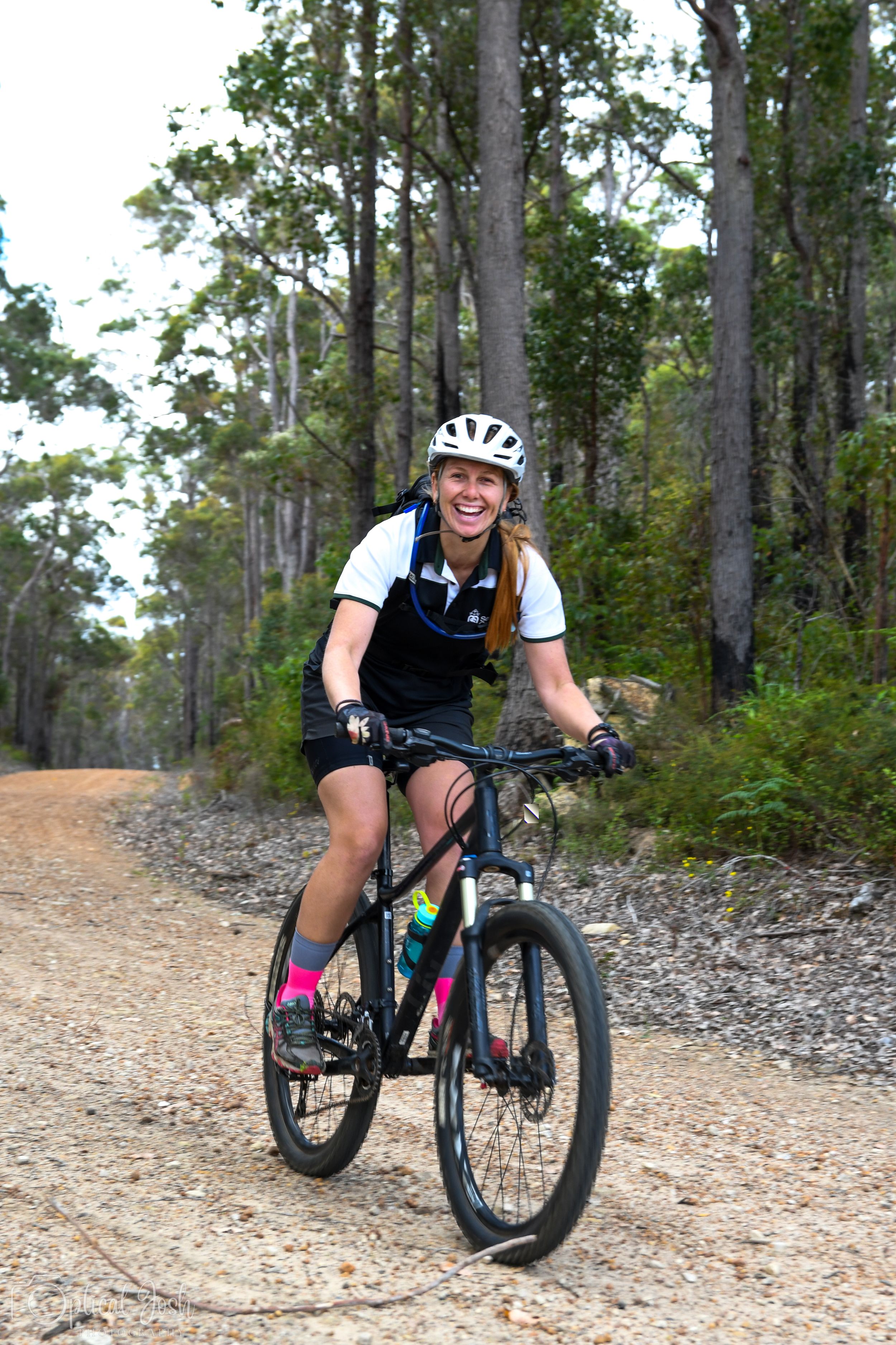 Mountain biker riding along a scenic forest trail on a black mountain bike wearing cycling gear.