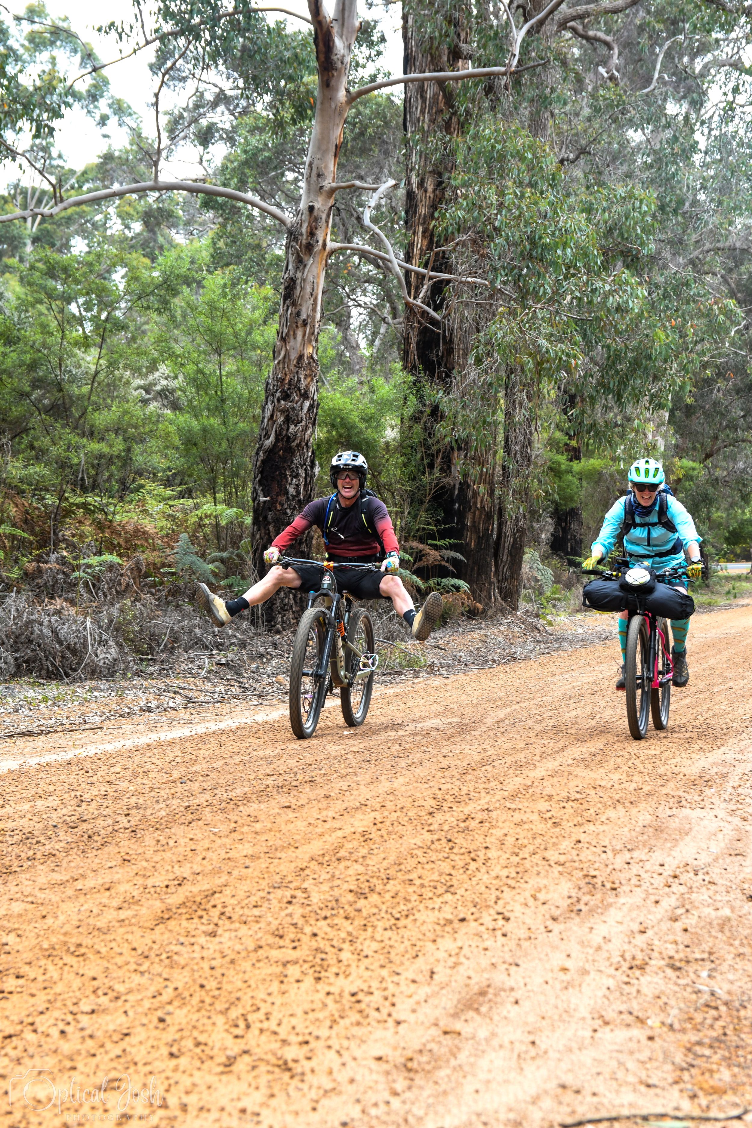 Two cyclists riding mountain bikes on a dirt trail through eucalyptus forest in Australia.