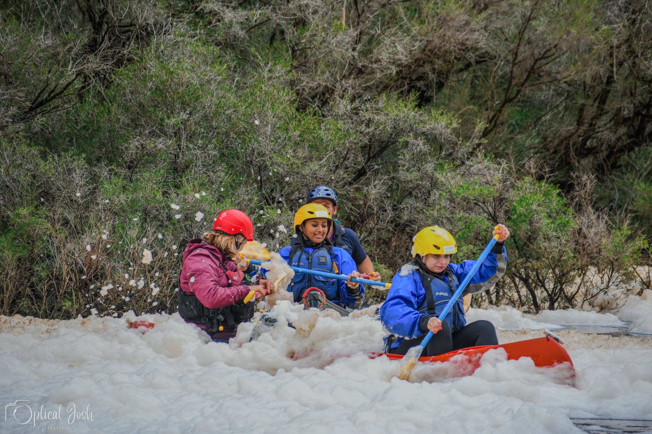 Three adventurous kayakers navigate through choppy white water rapids while wearing protective helmets and gear.