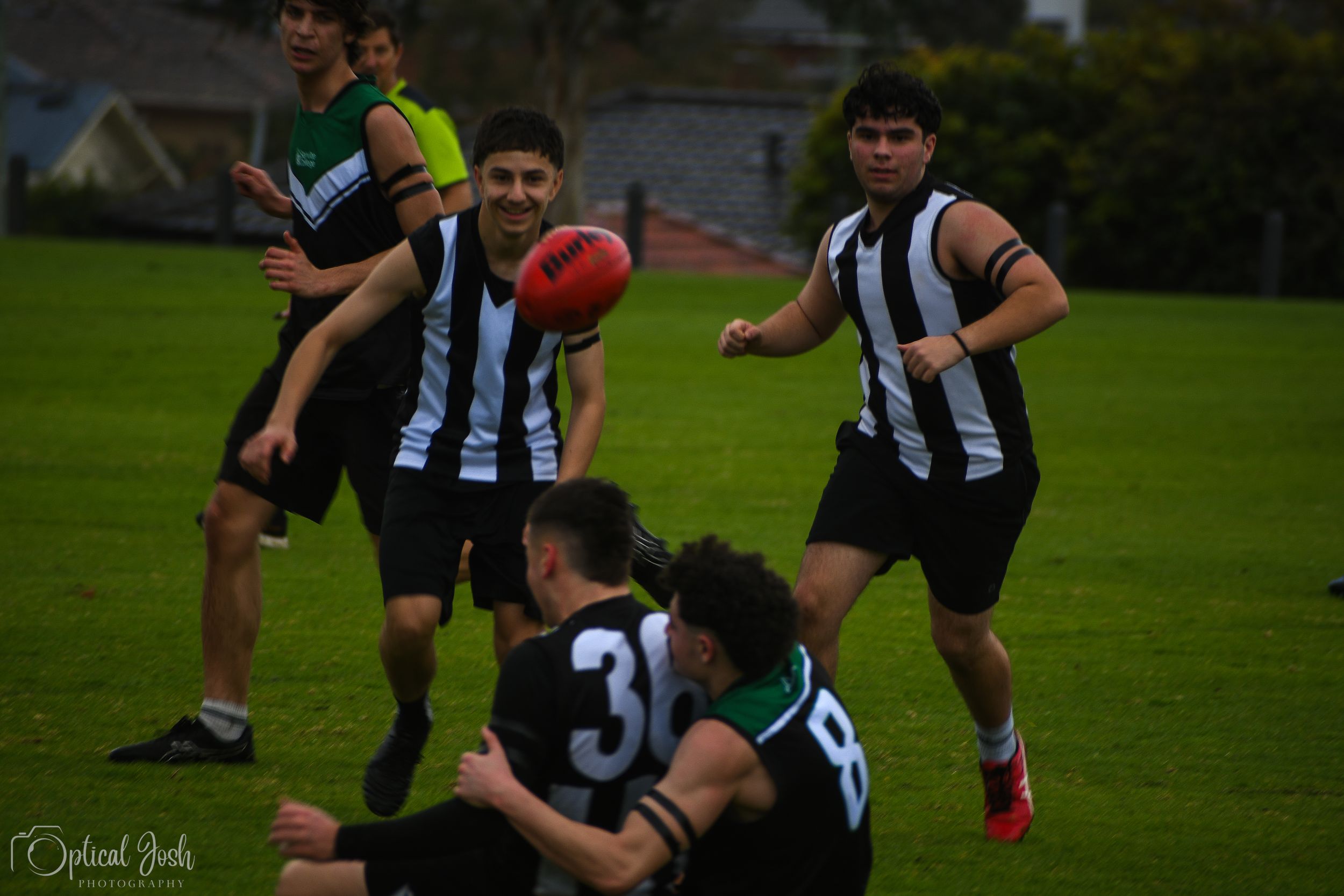 Australian Rules Football players in black and white striped jerseys compete for possession during a match.