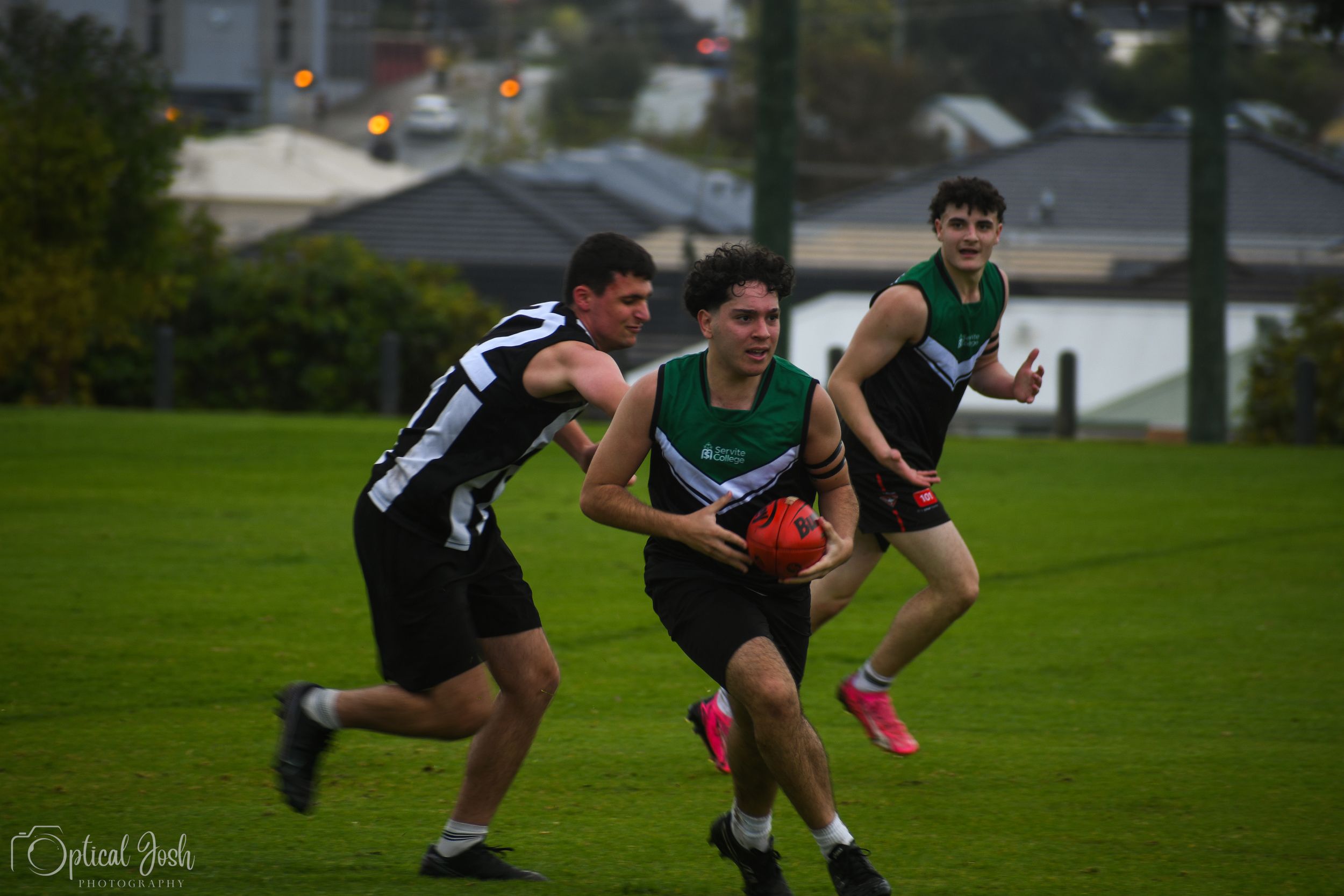 Australian rules football players compete for possession during a match on a wet grass field.