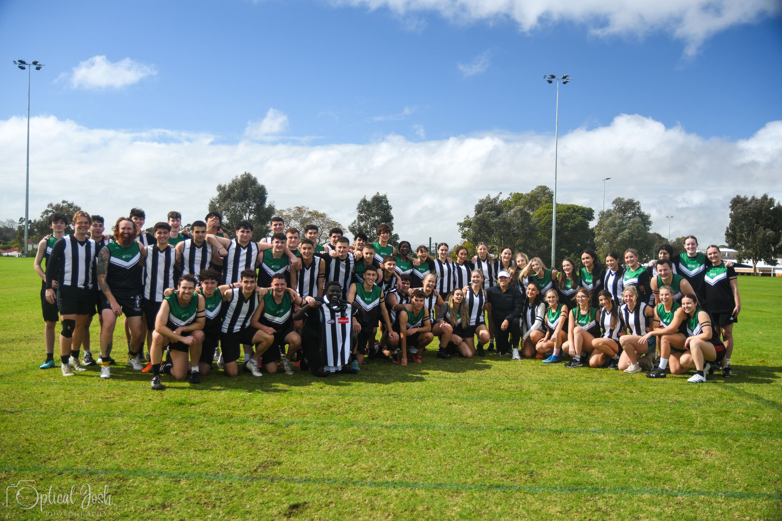 Sports team members in black and white striped uniforms gather for a group photo on a sunny day on green grass field.