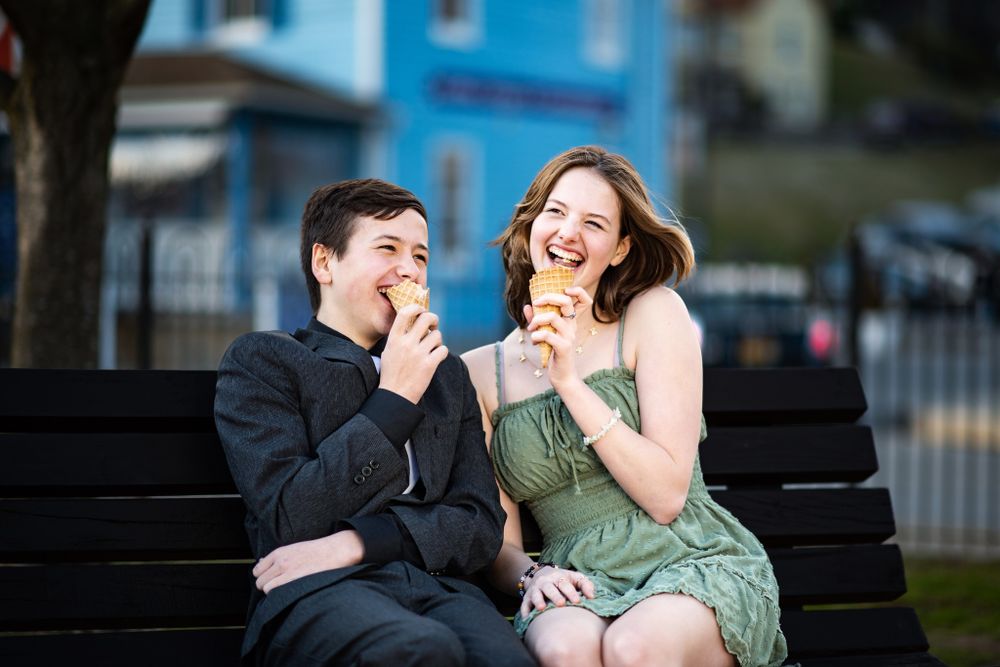 Two people sitting on a park bench and laughing together while sharing a happy moment outdoors.