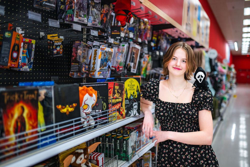 A customer in a polka dot dress browses board games and toys on retail store shelves.