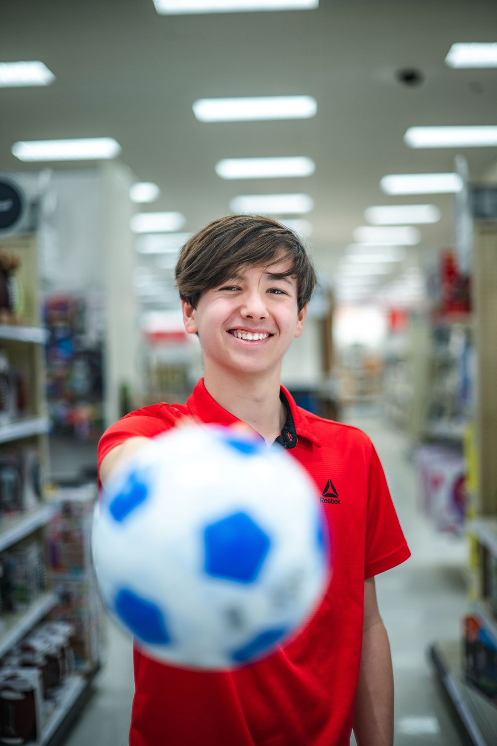A bright blue and white soccer ball floats in focus in front of store aisles with fluorescent lighting overhead.