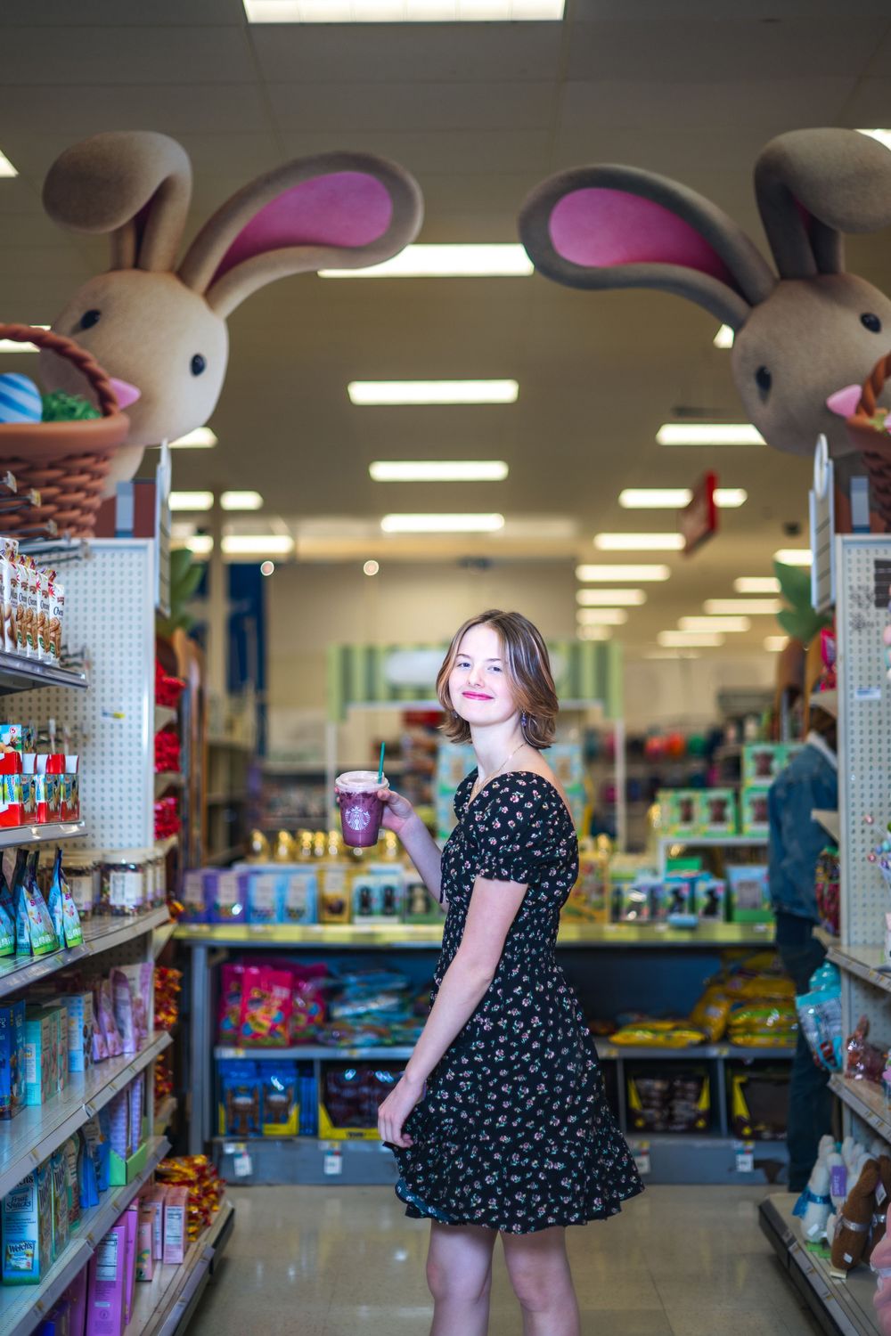 A person in a polka dot dress poses between Easter bunny decorations in a store aisle.
